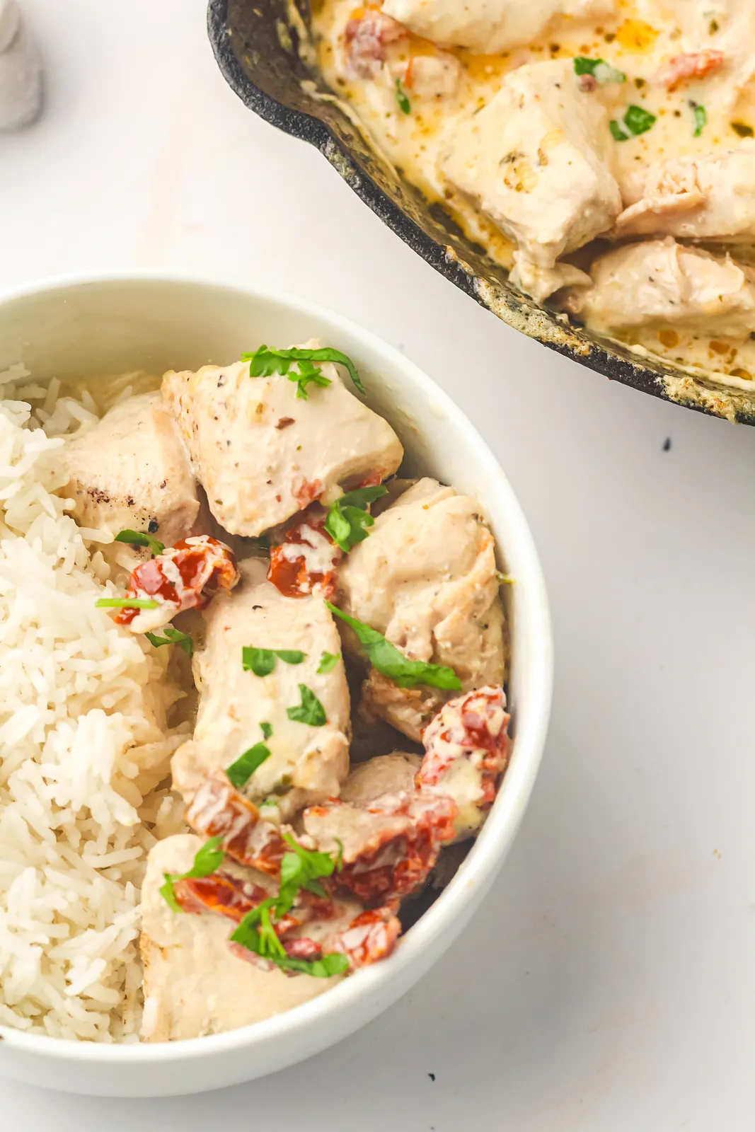 Marry me chicken over white rice in a bowl with the cast iron skillet behind
