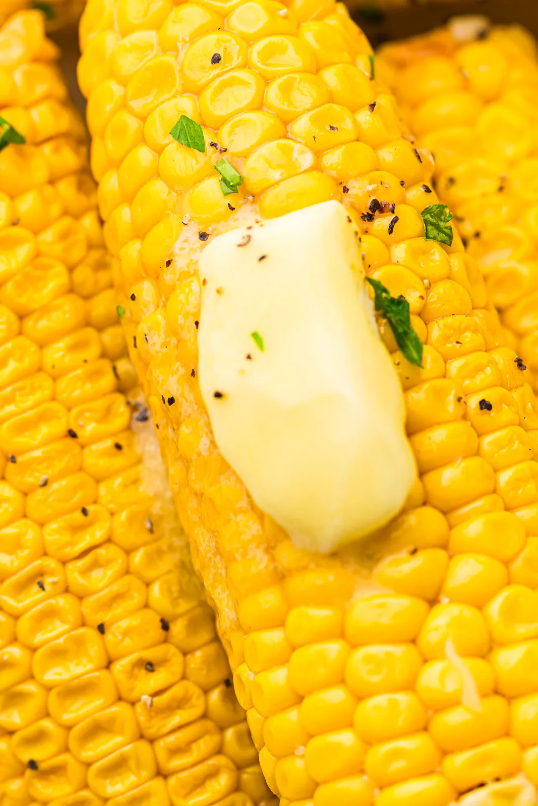 A pat of butter melting over golden kernels with black pepper and chopped parsley