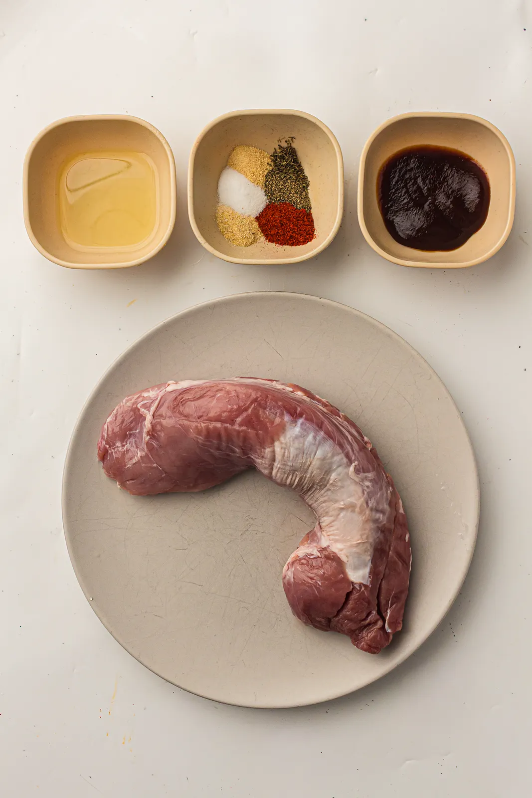 Ingredients for Ninja Woodfire pork tenderloin: raw tenderloin, oil, spice rub and BBQ sauce