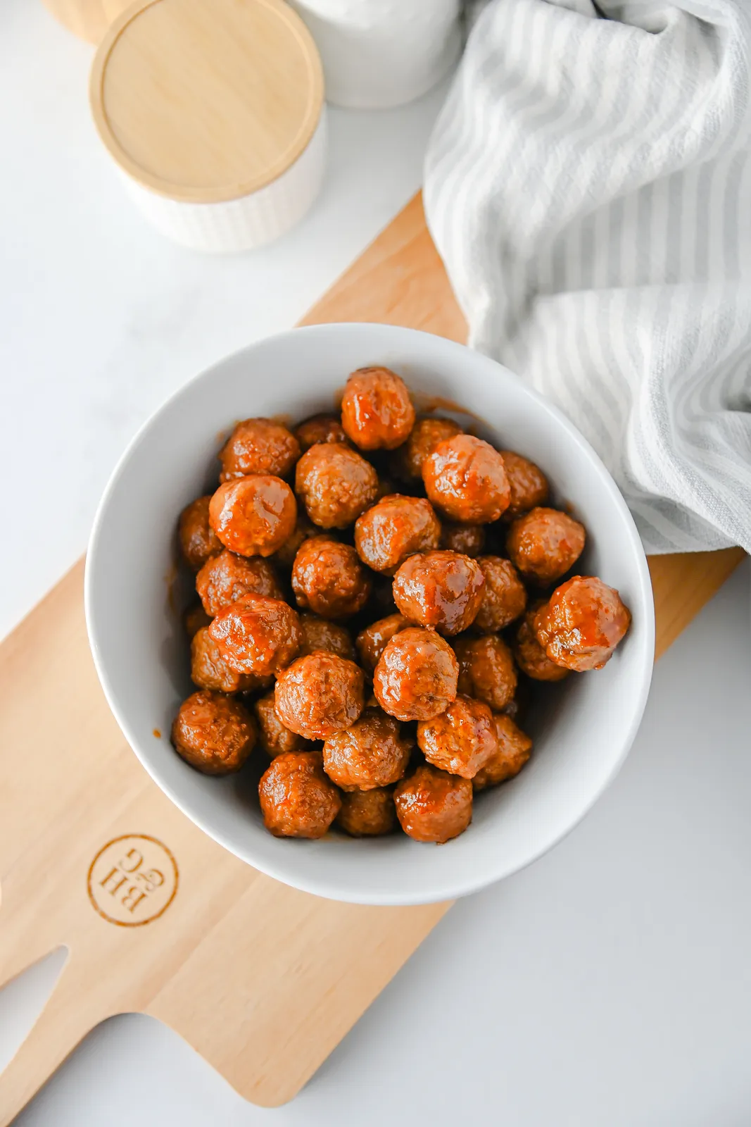 Overhead view of a bowl of glazed cocktail meatballs on a wooden paddle board
