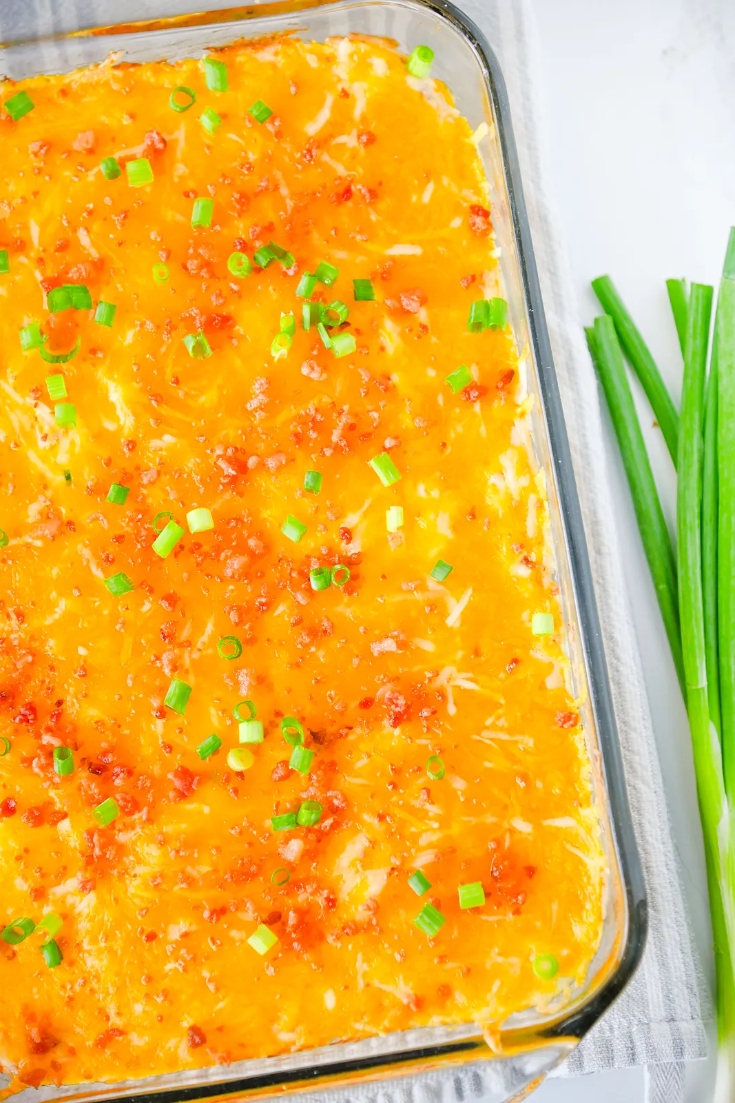 Overhead view of the whole cheesy ranch bake with spring onions laid beside the dish