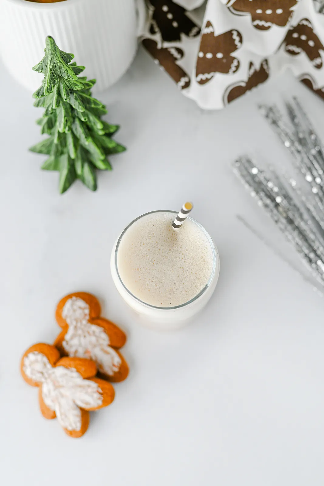 Overhead view of a frothy iced latte with a striped straw beside iced gingerbread men