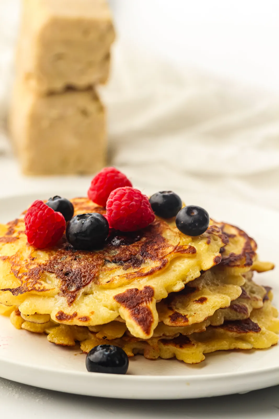 A golden short stack on a white plate topped with raspberries and blueberries