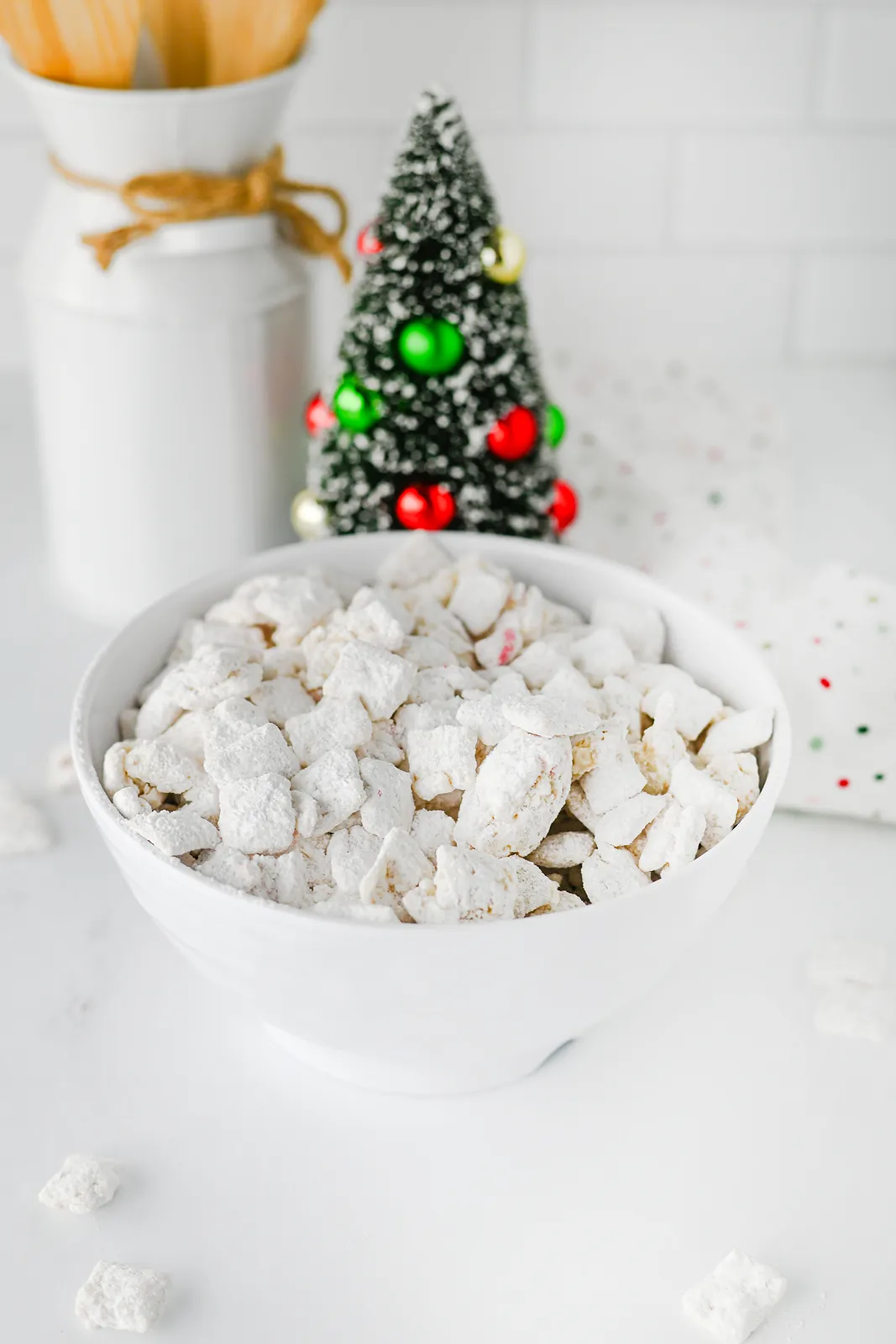 Peppermint puppy chow in a white bowl beside a little Christmas tree