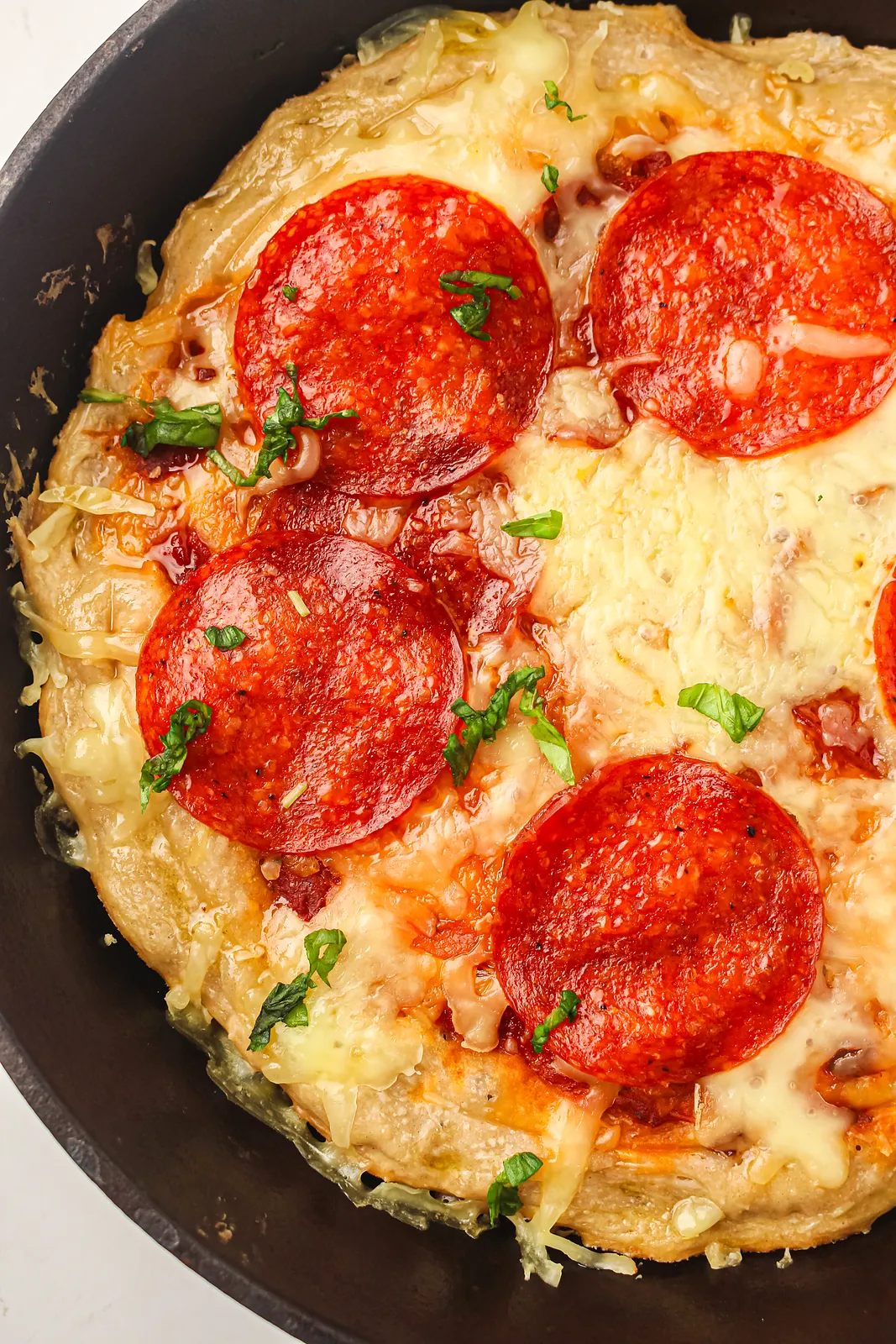 Close up of crisp pepperoni and fresh basil on bubbling mozzarella in a black pan