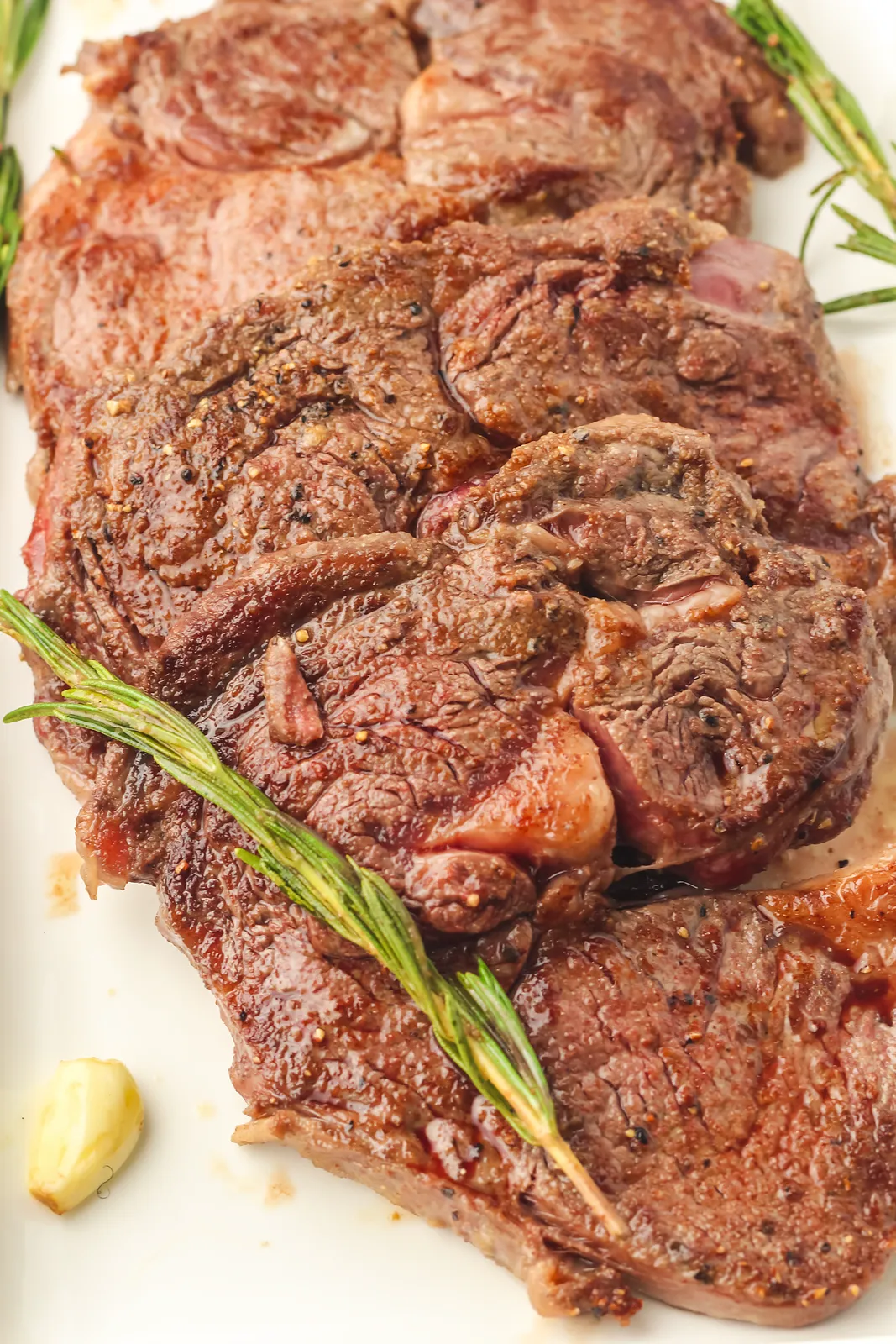 A pile of seared steaks on a plate with rosemary sprigs and garlic