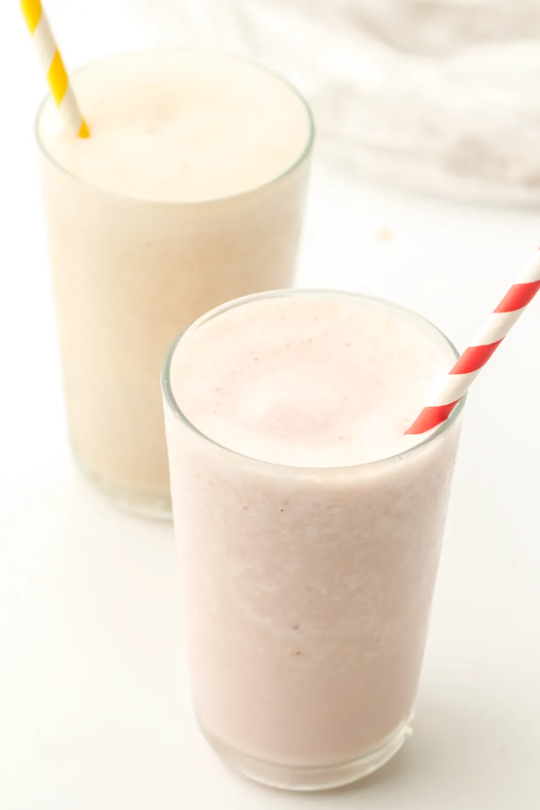 Tall glasses of pink and cream blended drinks with striped paper straws