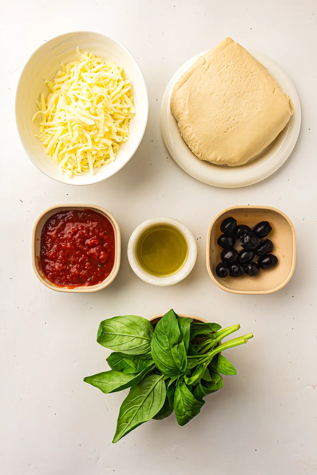 Ingredients for pizza muffins: pizza dough, shredded mozzarella, pizza sauce, olive oil, black olives and fresh basil