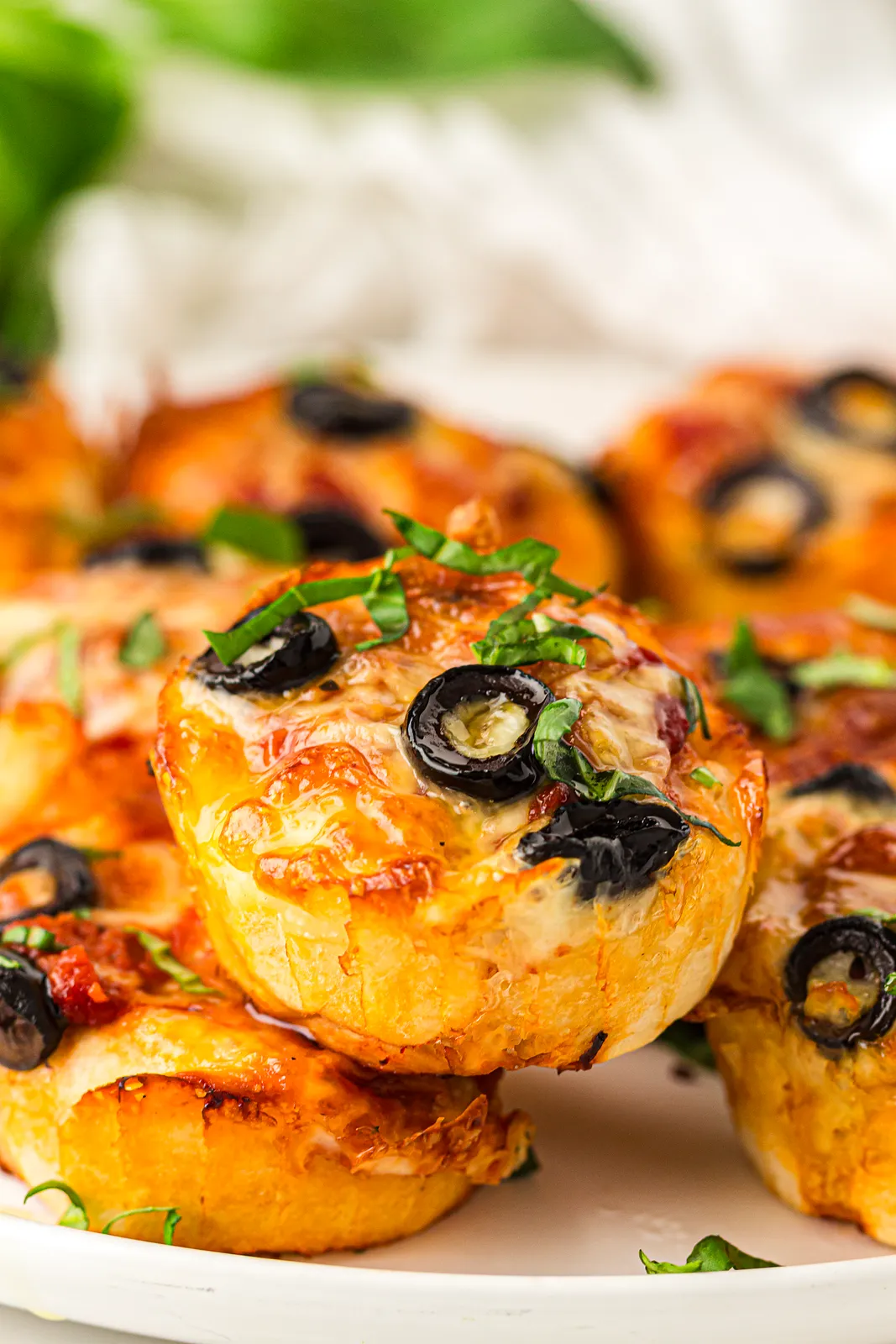 Pizza muffins topped with black olives and fresh basil on a white plate