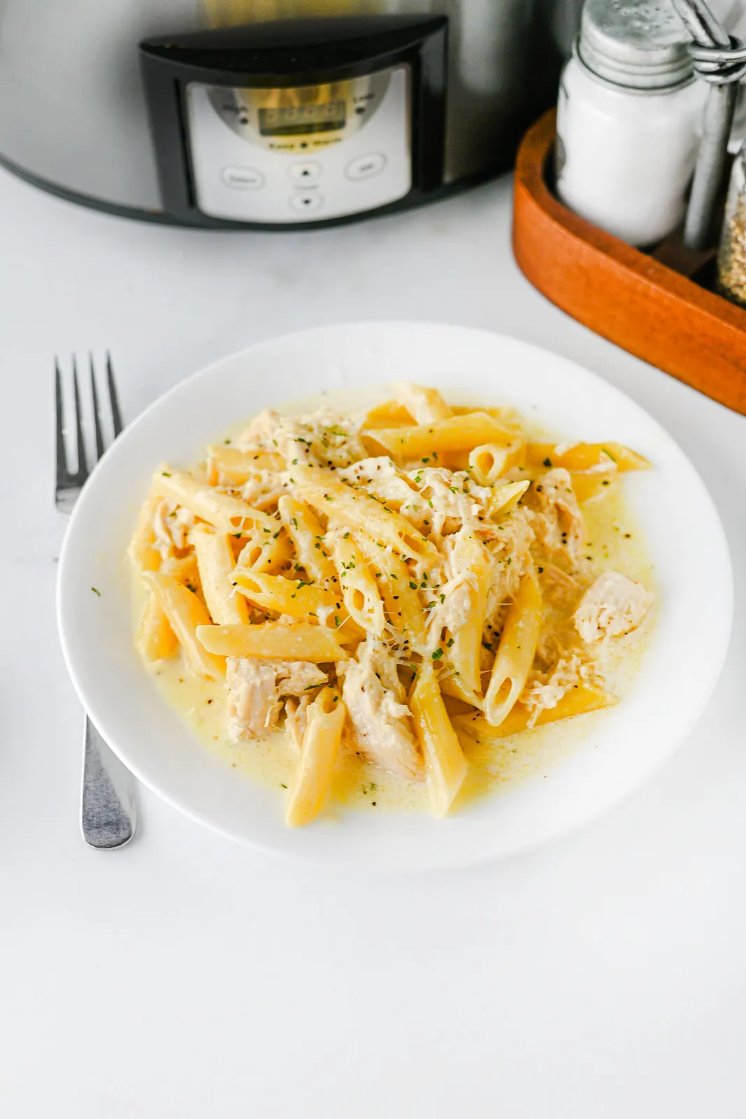 A plate of shredded chicken penne in cream sauce with parsley and a fork
