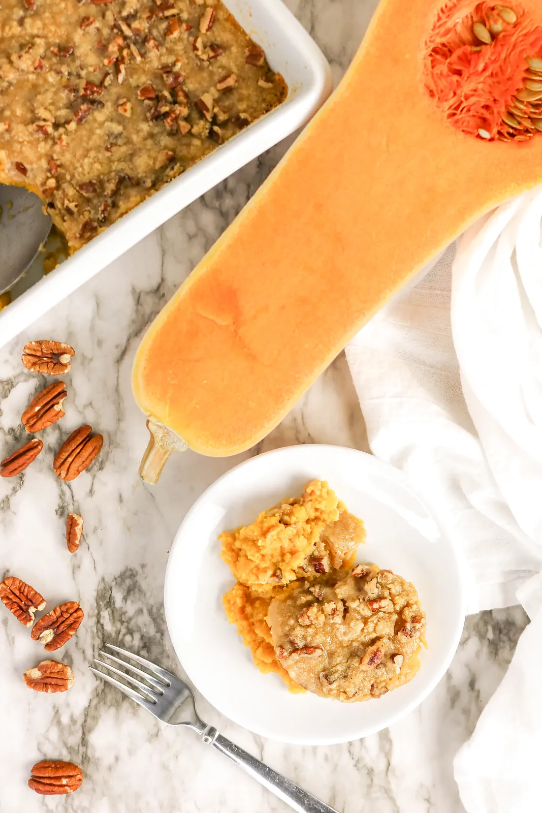 A small plate of the sweet orange bake beside a halved gourd and scattered pecans