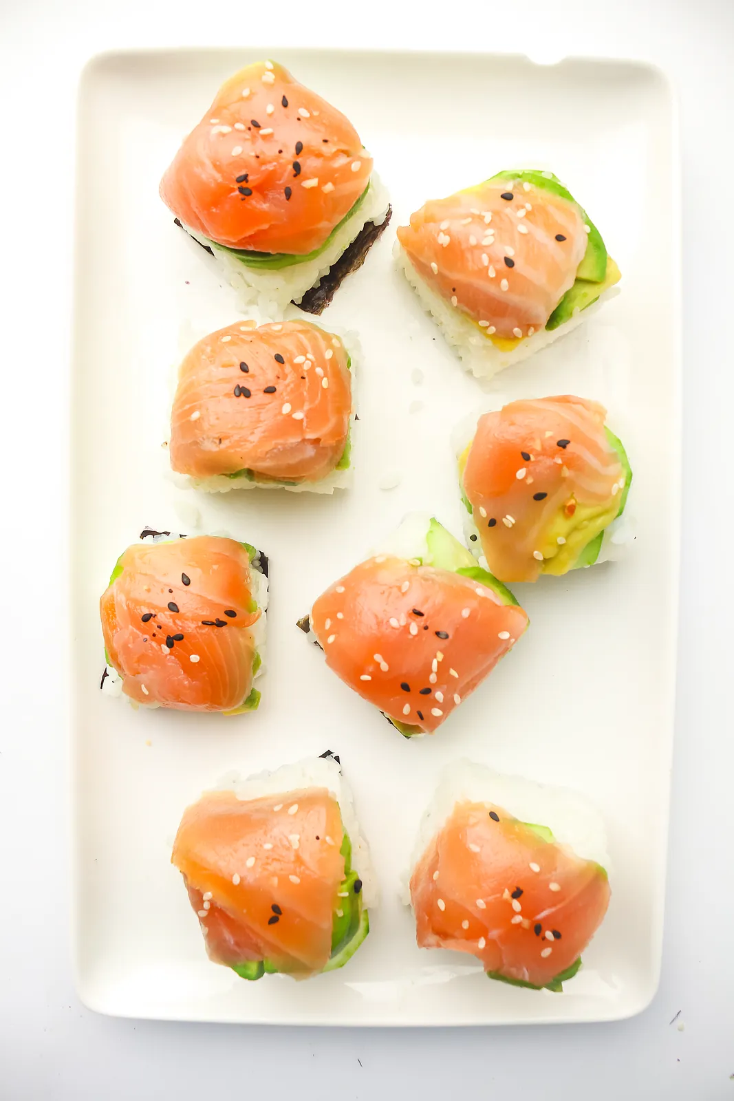 Eight salmon topped rice bites with sesame seeds arranged on a long white platter