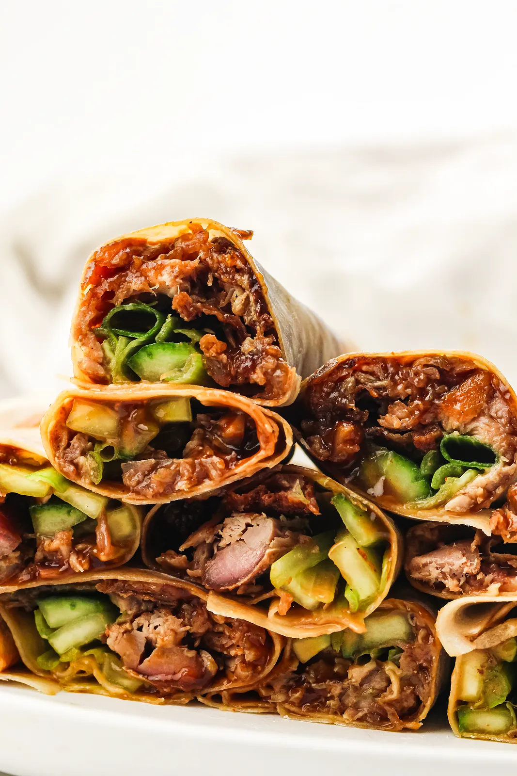 A platter of rolled wraps stacked two high with glossy hoisin at the ends