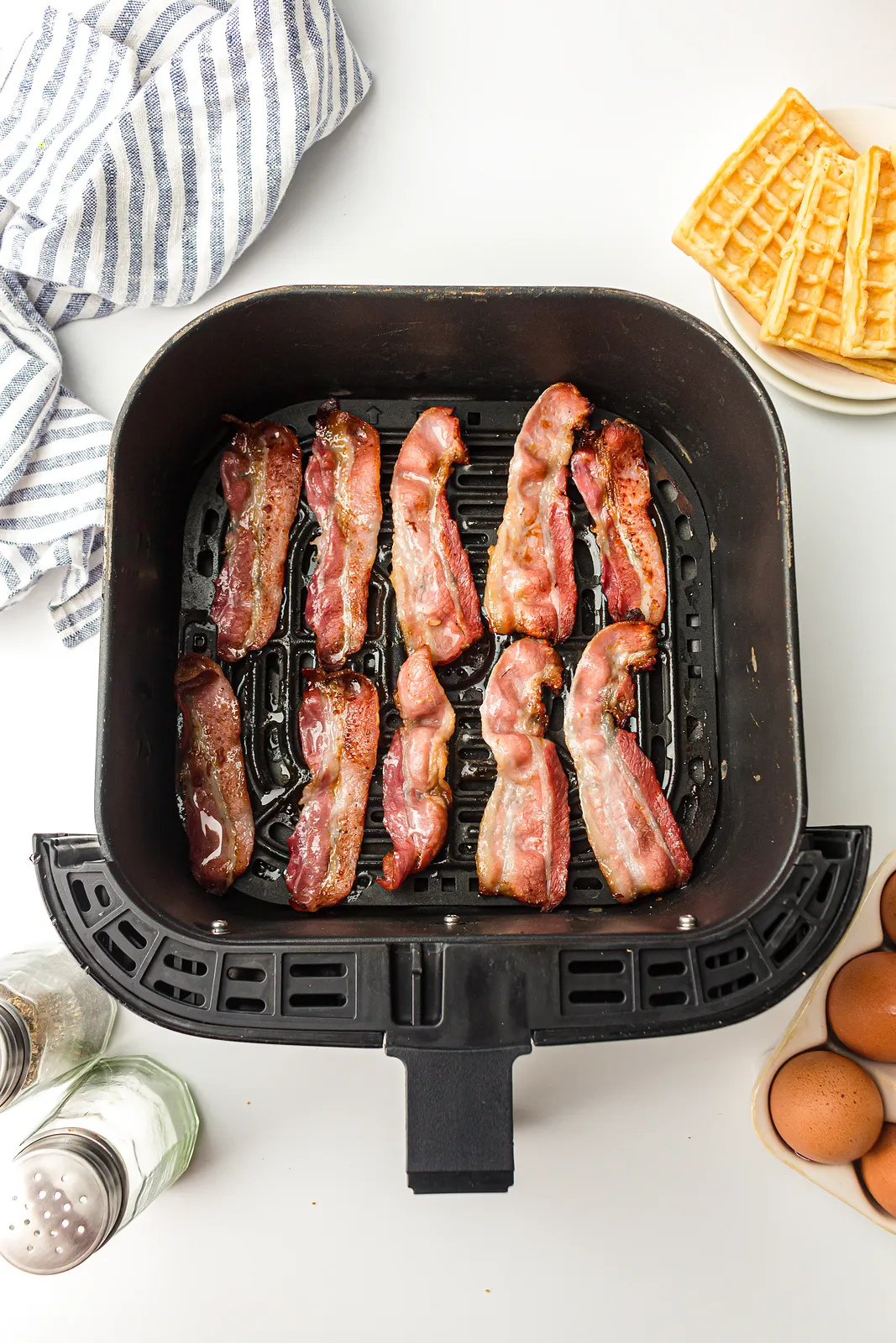 Golden cooked rashers lying in a black basket next to eggs and a waffle