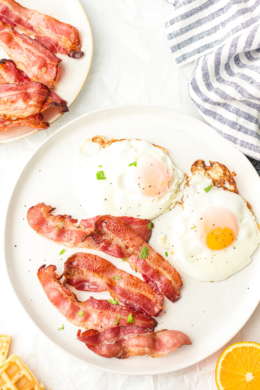 Crisp rashers next to two fried eggs on a white plate with orange halves