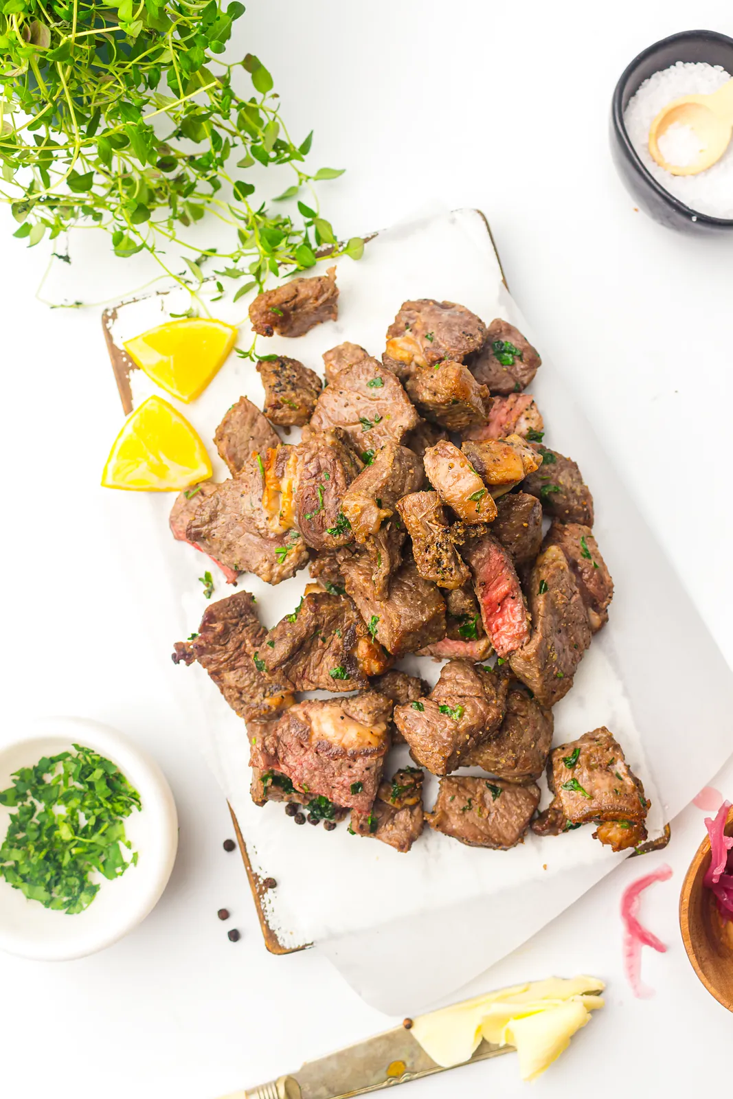 Seared ribeye cubes piled on parchment with lemon wedges, chopped parsley and flaky salt
