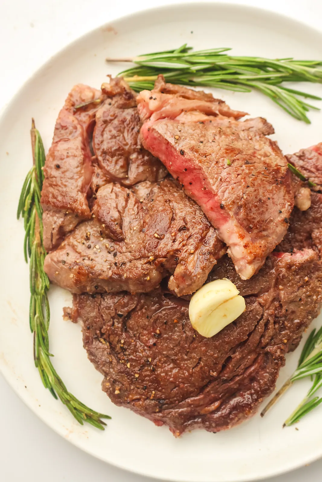 Ribeye on Blackstone, seared and served on a white plate with garlic and rosemary