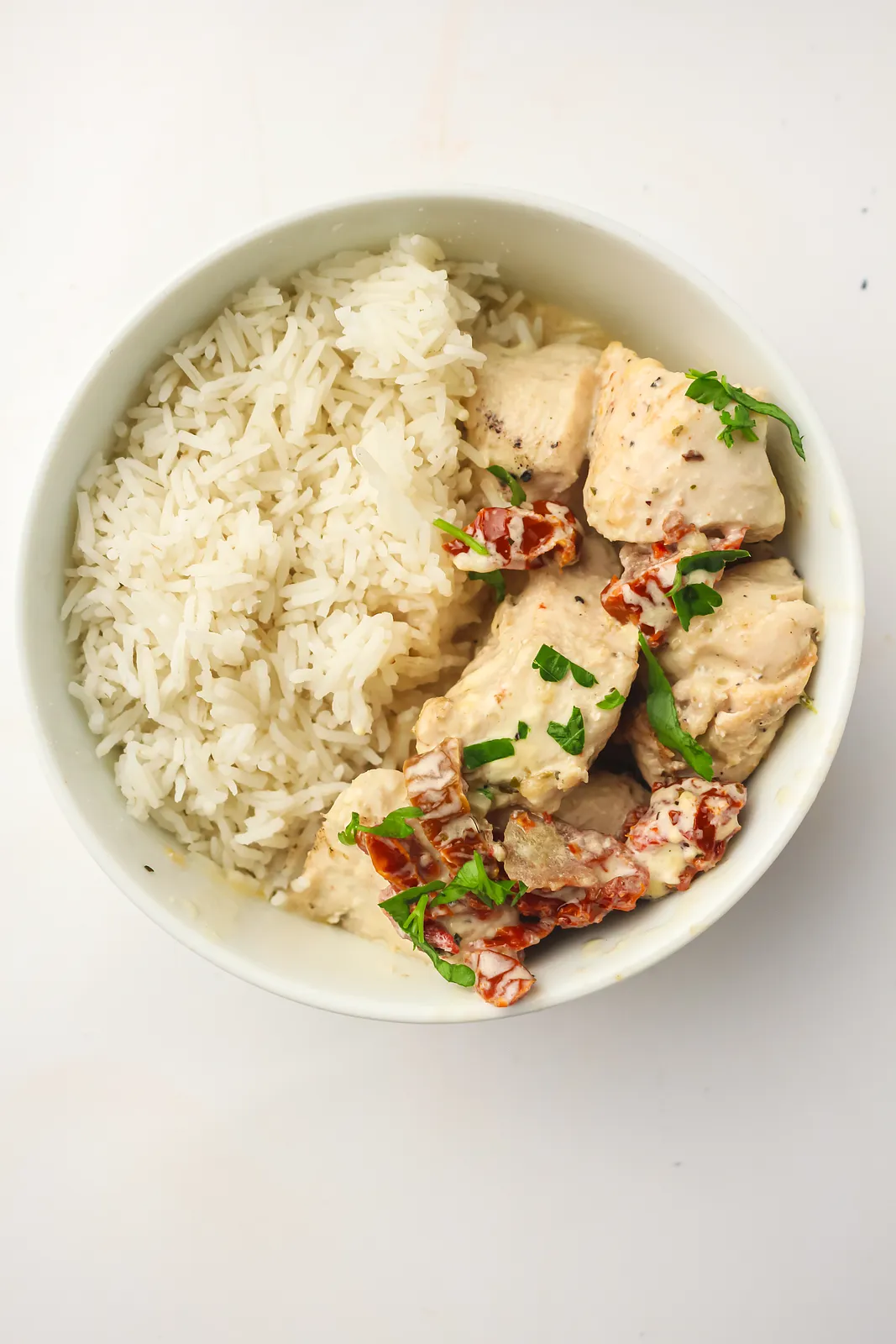 Overhead view of a rice bowl topped with seared pieces, sun-dried tomatoes and herbs