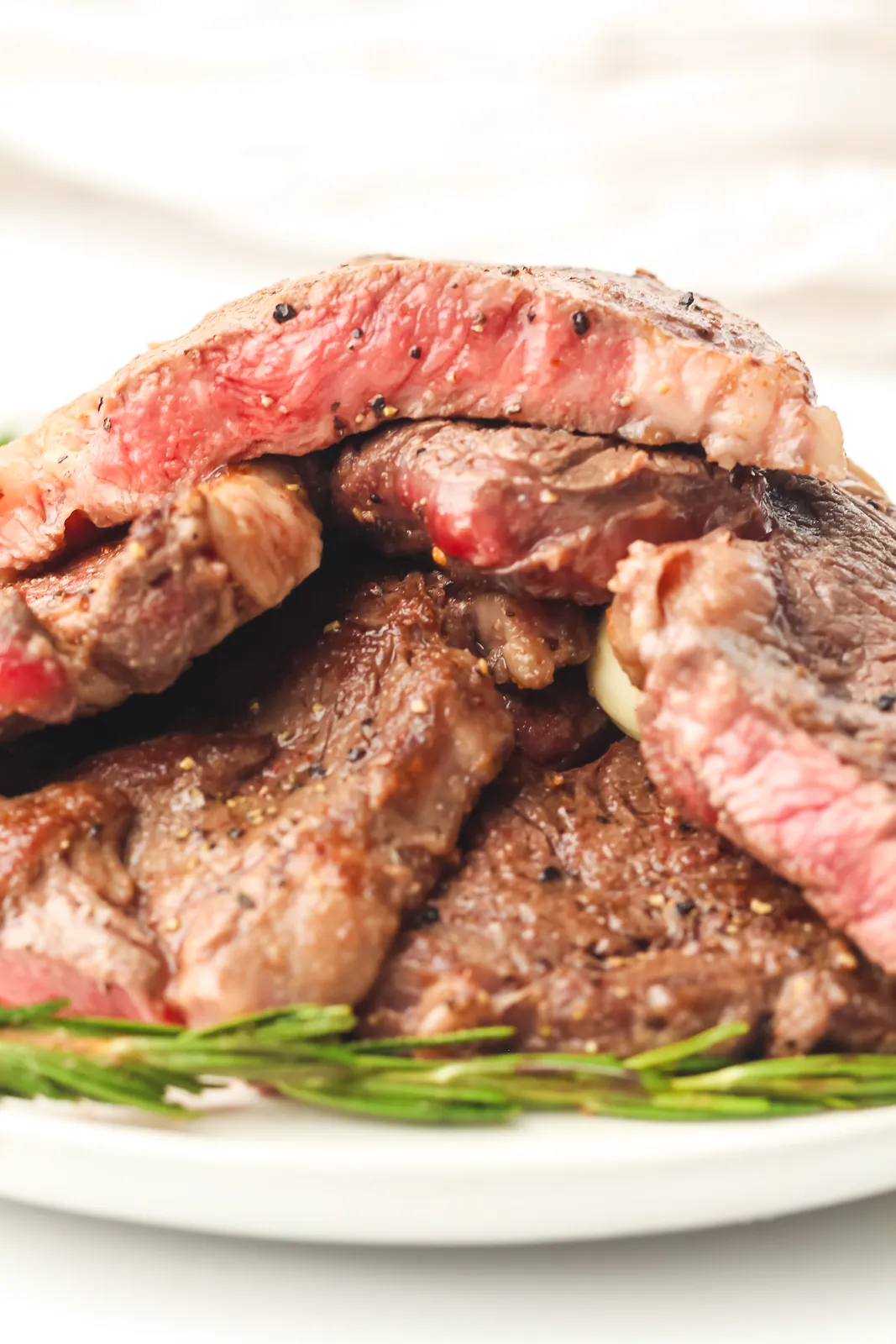 Rosy pink steak slices piled on a plate with rosemary
