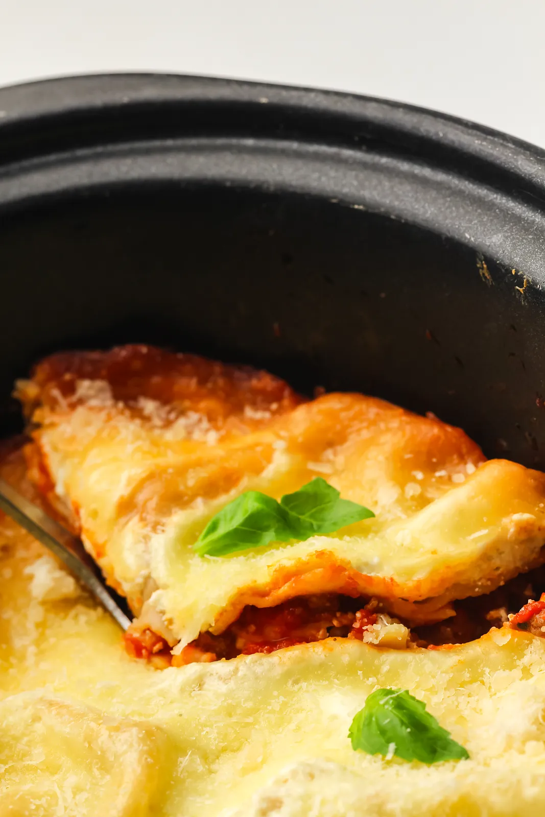 A wedge being served from the slow cooker pot with melted mozzarella and basil