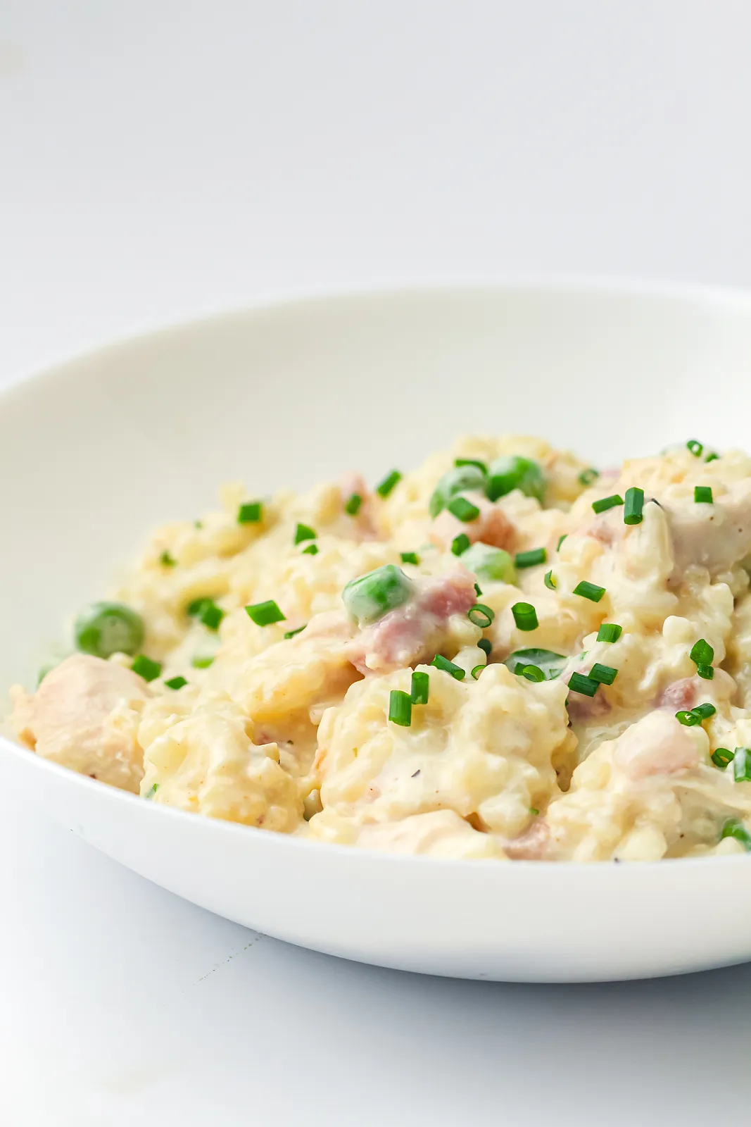 Side view of a shallow white bowl of creamy rice, peas and pieces of bacon