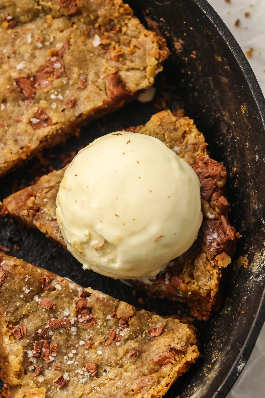 Brown butter skillet cookie cut into wedges in a cast iron pan with a scoop of vanilla ice cream