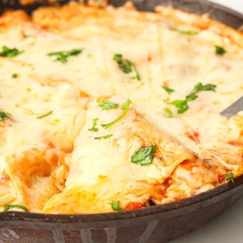 Skillet lasagna in a cast iron pan with melted mozzarella and fresh parsley, one wedge cut