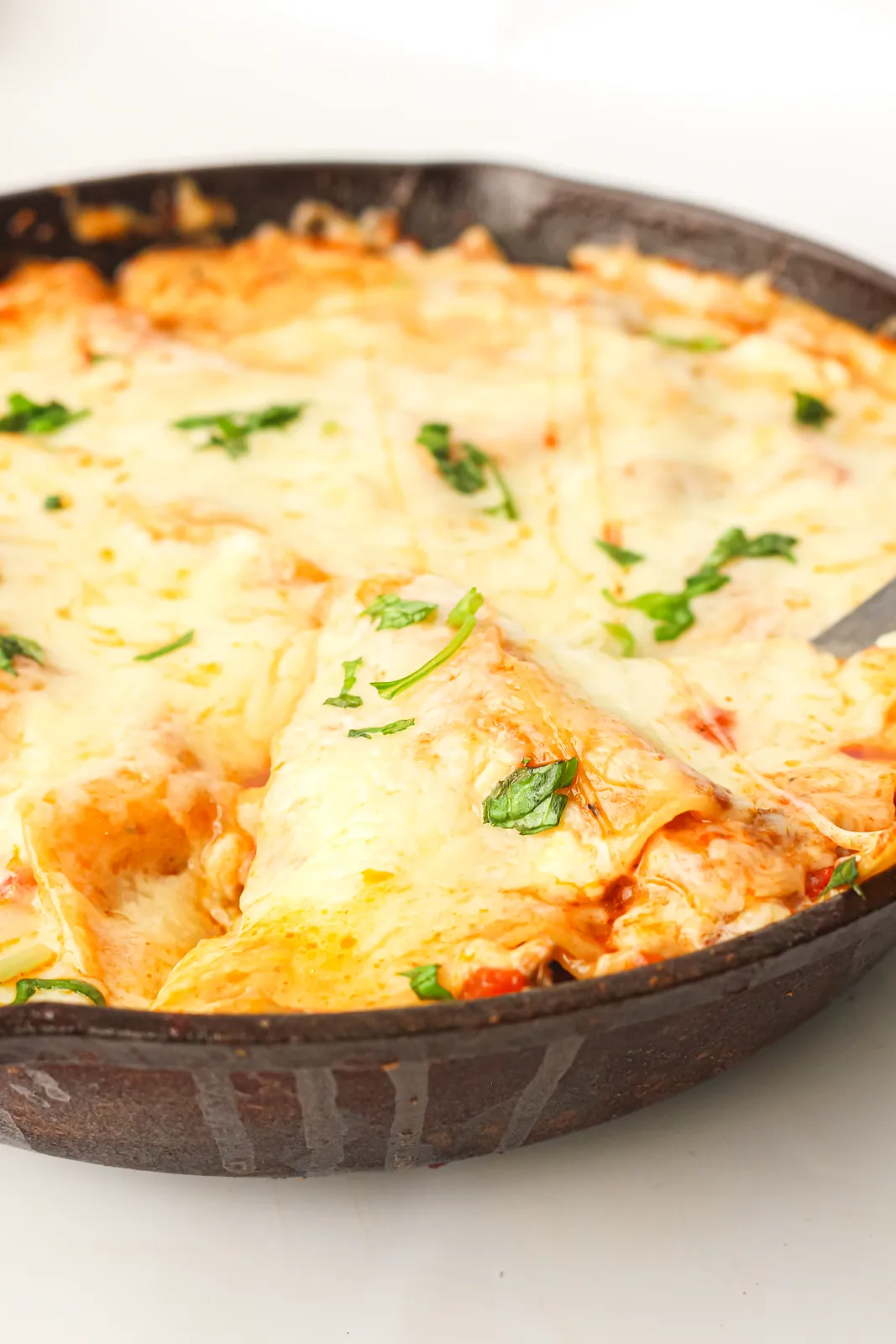 Melted mozzarella and ricotta over beef ragu and pasta in a cast iron pan with one wedge cut