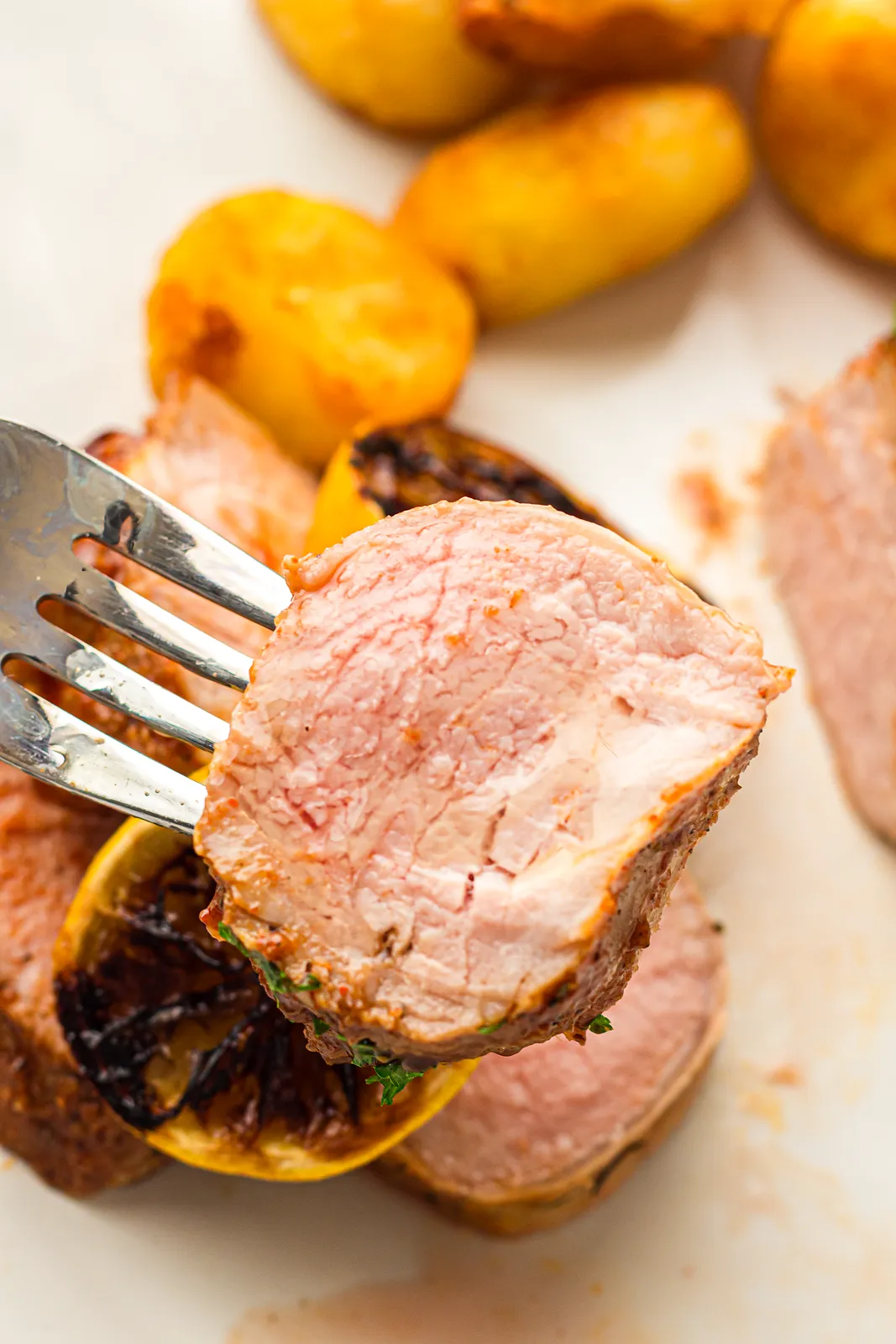 A slice lifted on a fork over crispy roast potatoes and a charred lemon