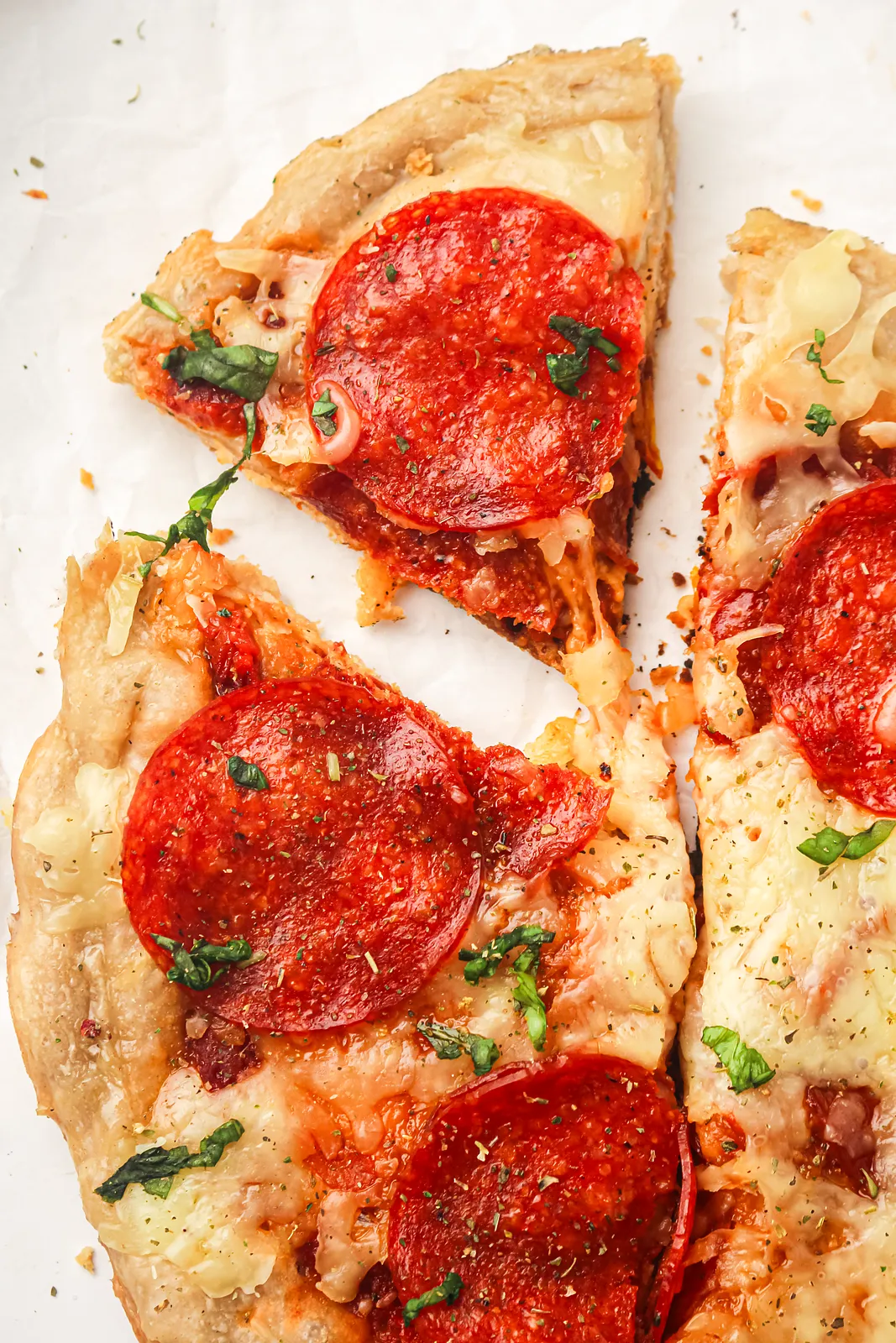 Pepperoni wedges cut and pulled apart on white parchment