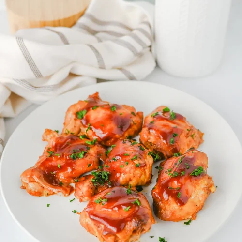 Slow cooker BBQ chicken thighs piled on a white plate with extra sauce and parsley