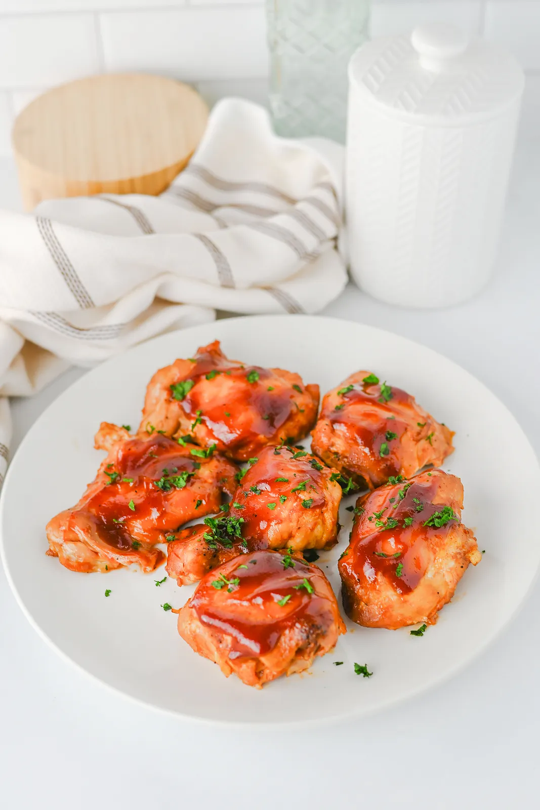 Slow cooker BBQ chicken thighs piled on a white plate with extra sauce and parsley