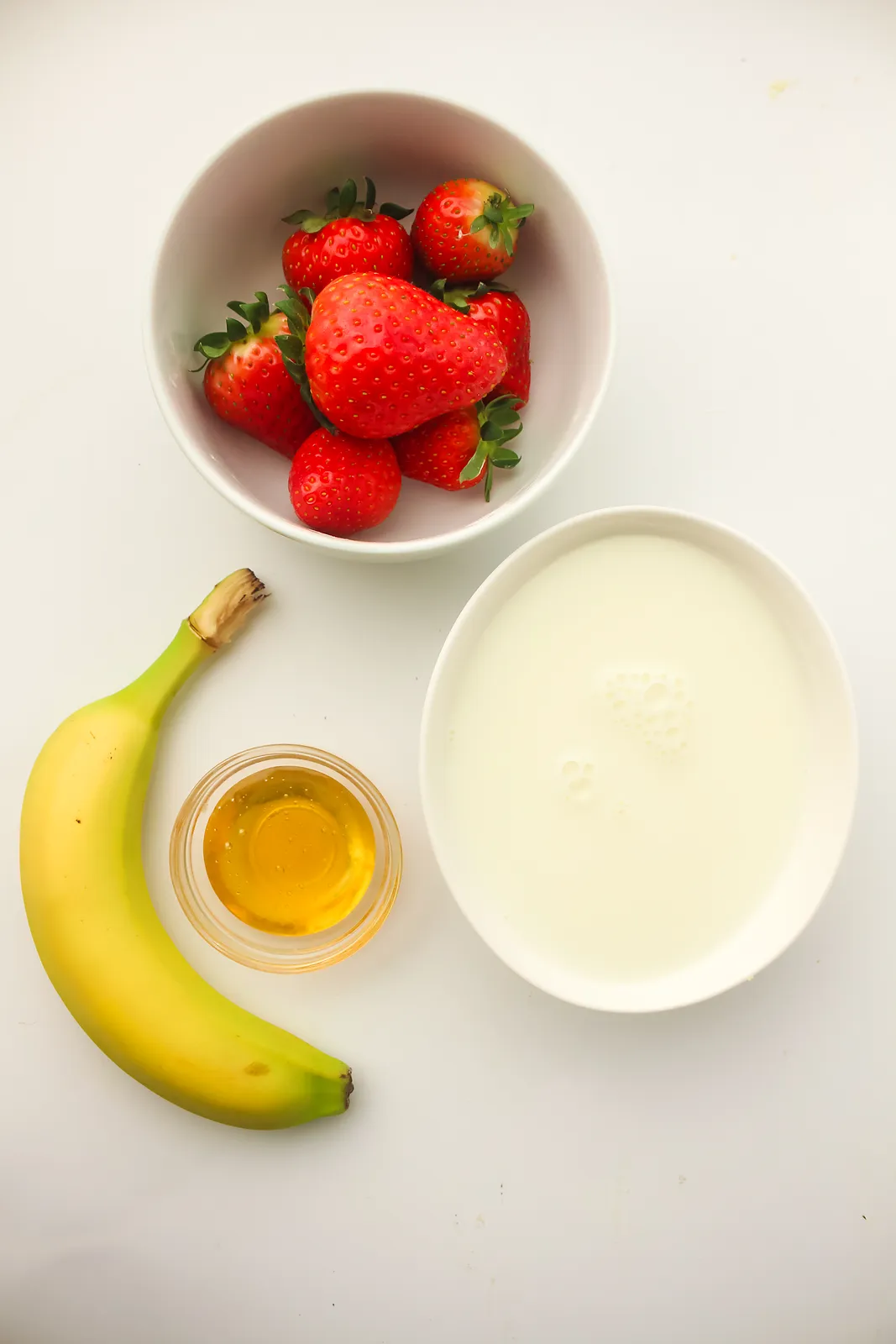 Ingredients for smoothie cubes: fresh strawberries, a ripe banana, honey and oat milk