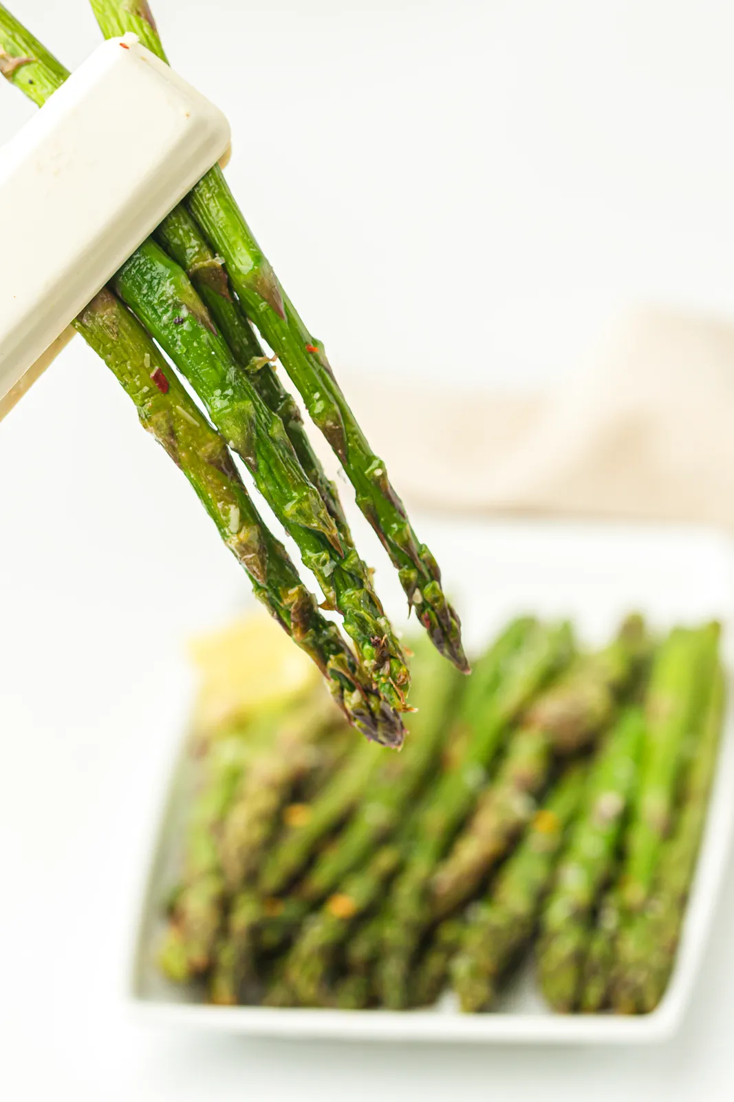 Cooked green spears being lifted with white tongs from a serving plate