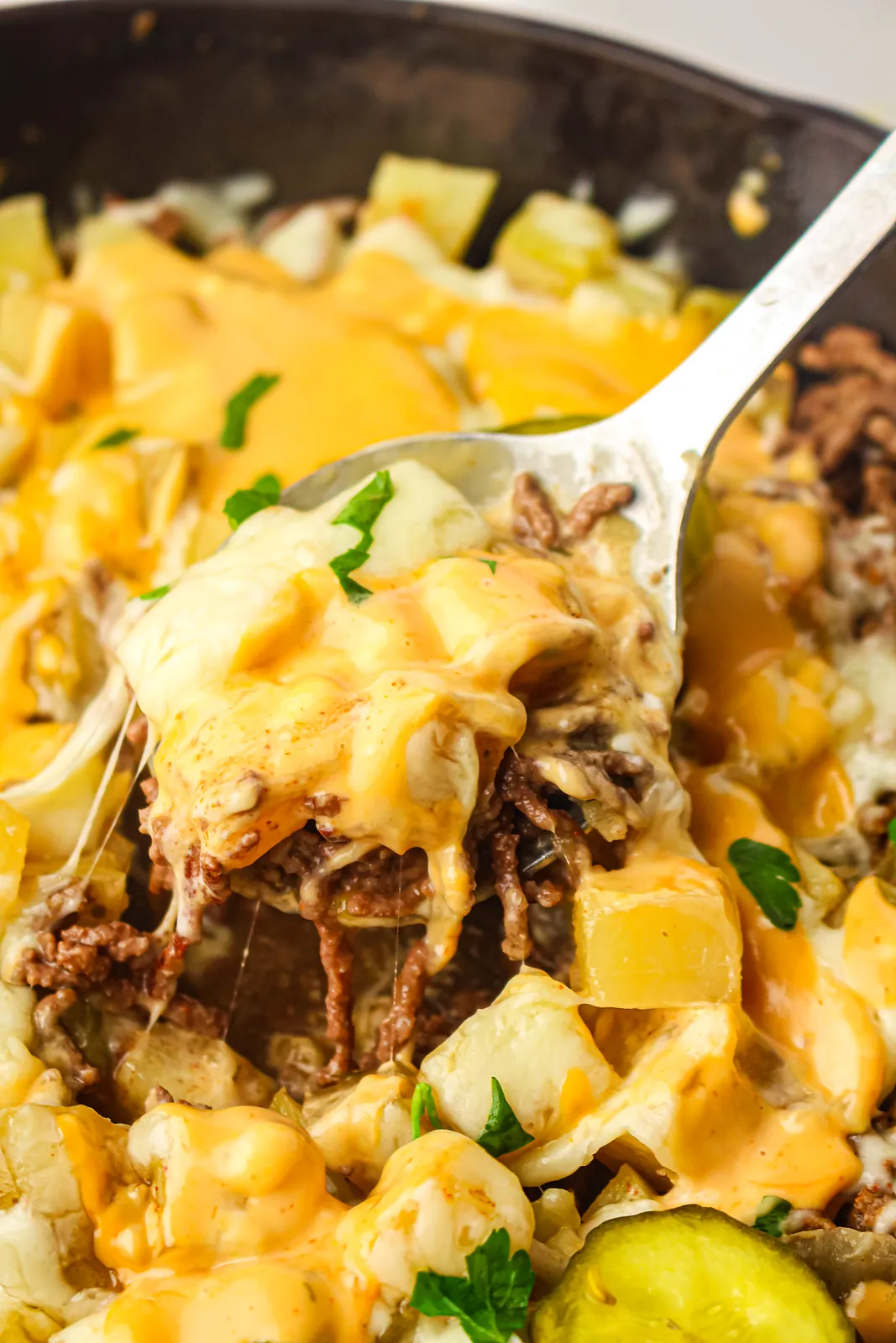 A spoonful of cheesy beef and potatoes lifted from the pan with stretchy melted cheese