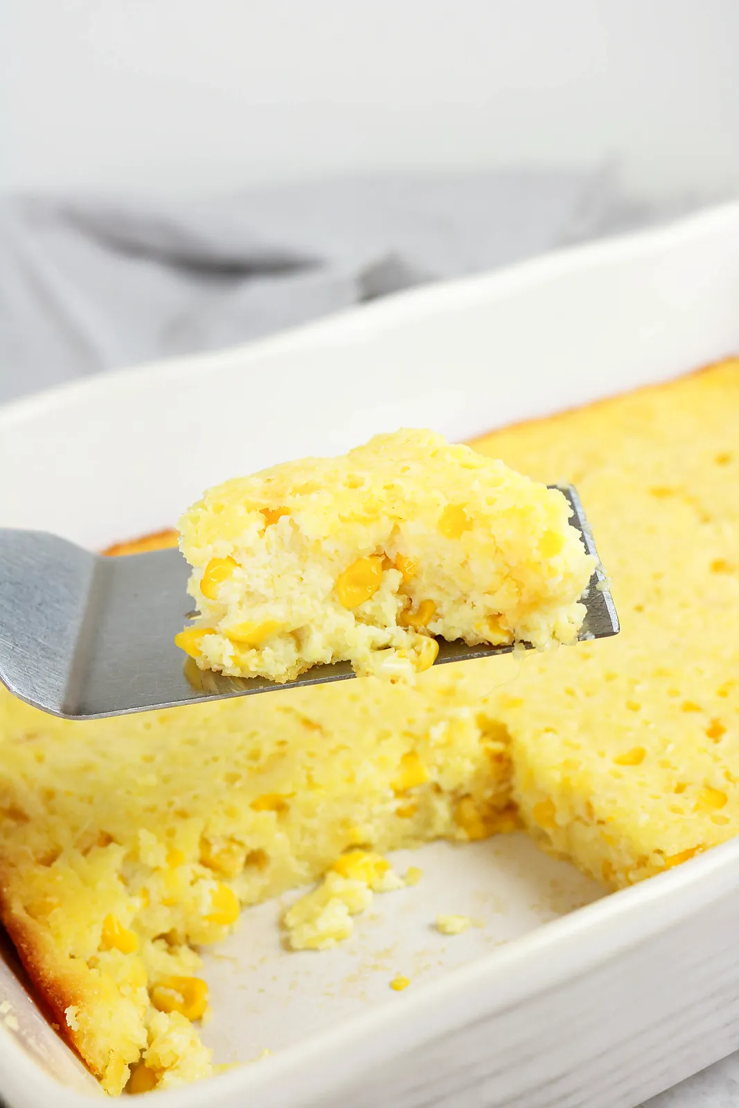 A soft, custardy portion full of yellow kernels held on a spatula above the dish