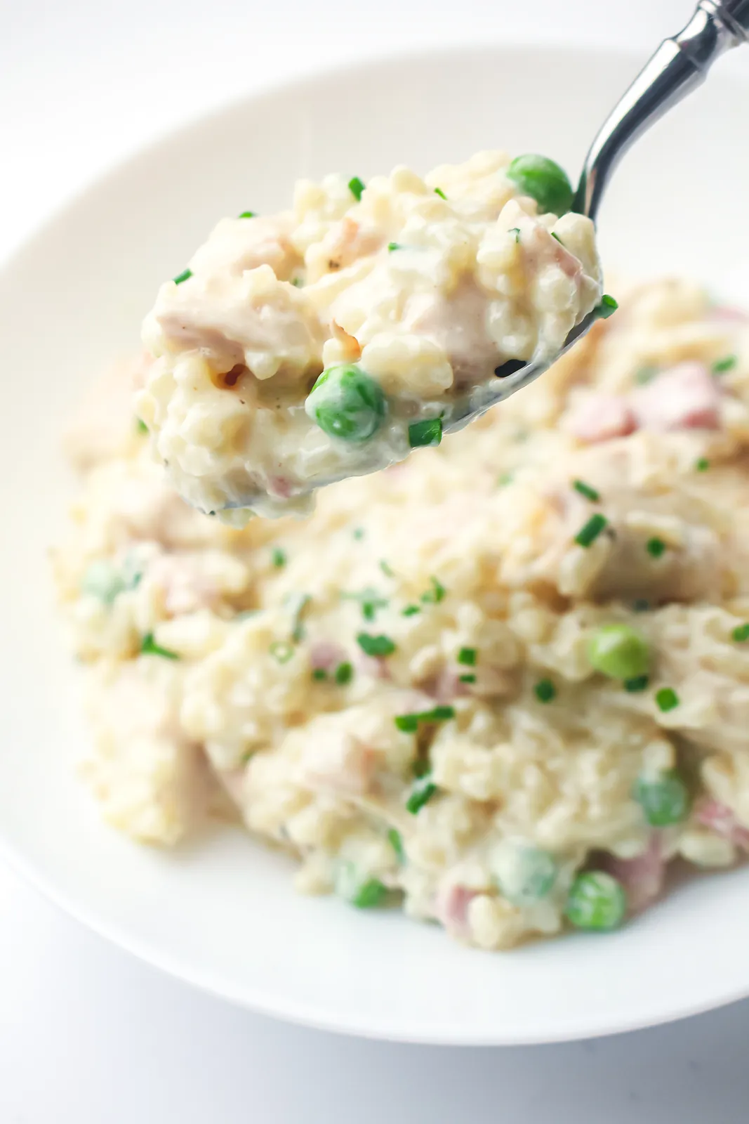 A spoonful of creamy rice with peas and bacon lifted from the bowl