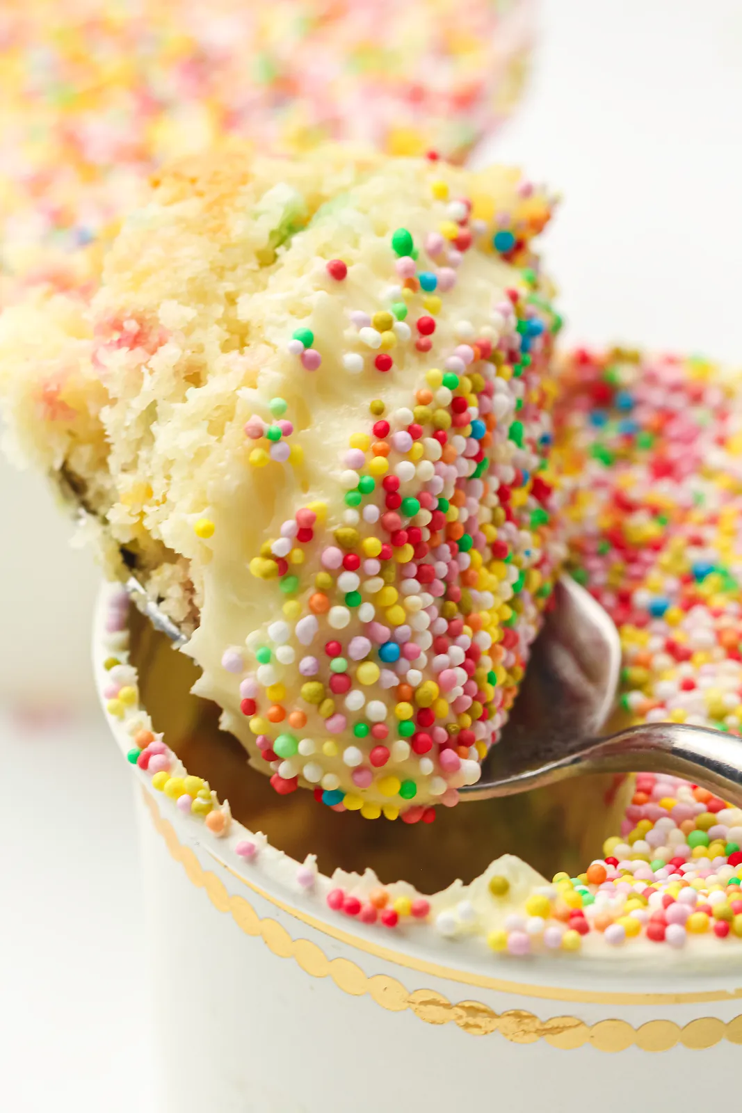 A spoon lifting funfetti sponge and vanilla frosting coated in sprinkles