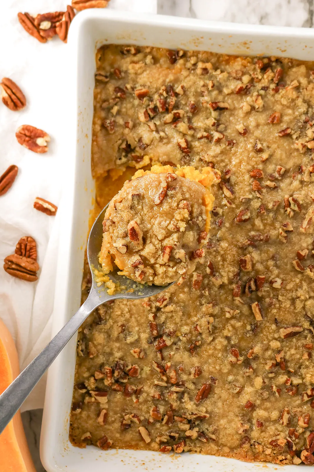 A metal spoon lifting a scoop of the pecan topped bake from the dish