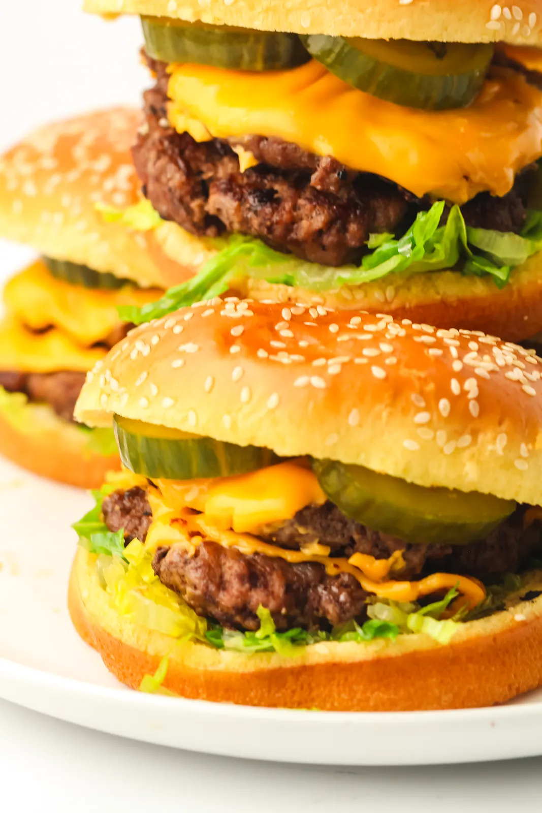 Two cheeseburgers stacked on a white plate with lettuce, pickles and melted cheese