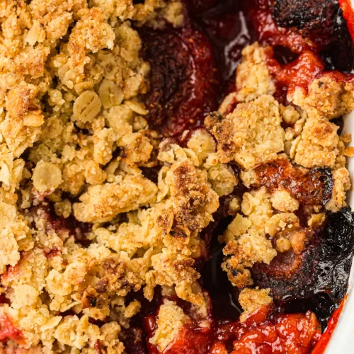 Strawberry crumble baked in a white dish with a golden oat topping and bubbling red fruit