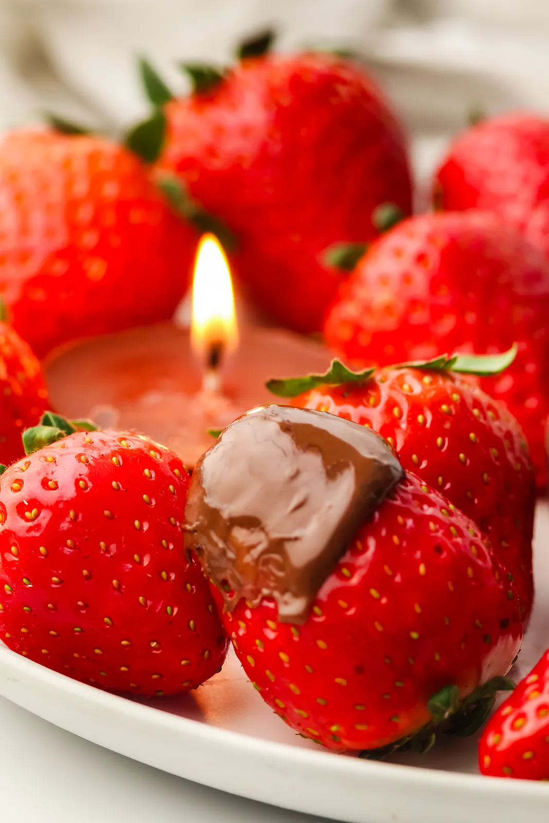 A strawberry dipped in warm melted chocolate on a plate of berries