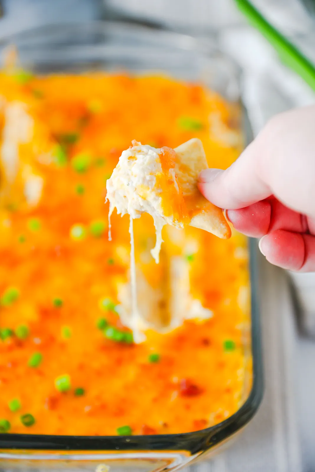 A tortilla chip lifting a stretchy, cheesy scoop from the baking dish
