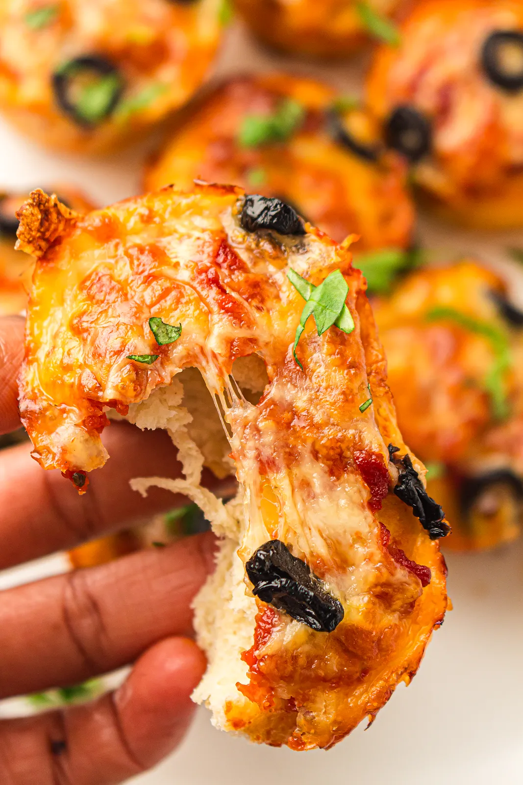 Stretchy melted mozzarella pulled from a torn dough cup with olives