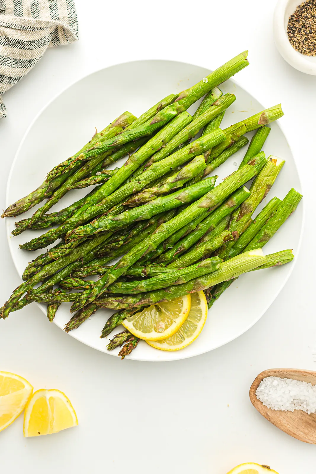Tender crisp green spears on a white plate with lemon slices and a pinch of salt