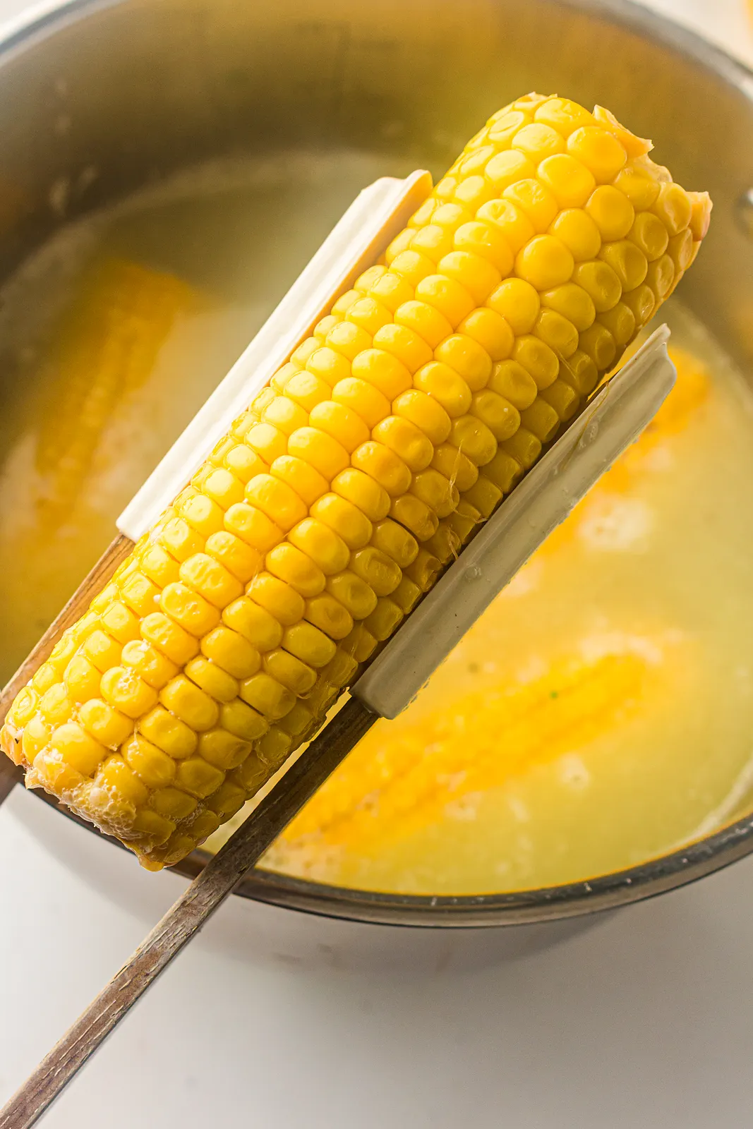 Tongs lifting a golden ear out of a steaming pot