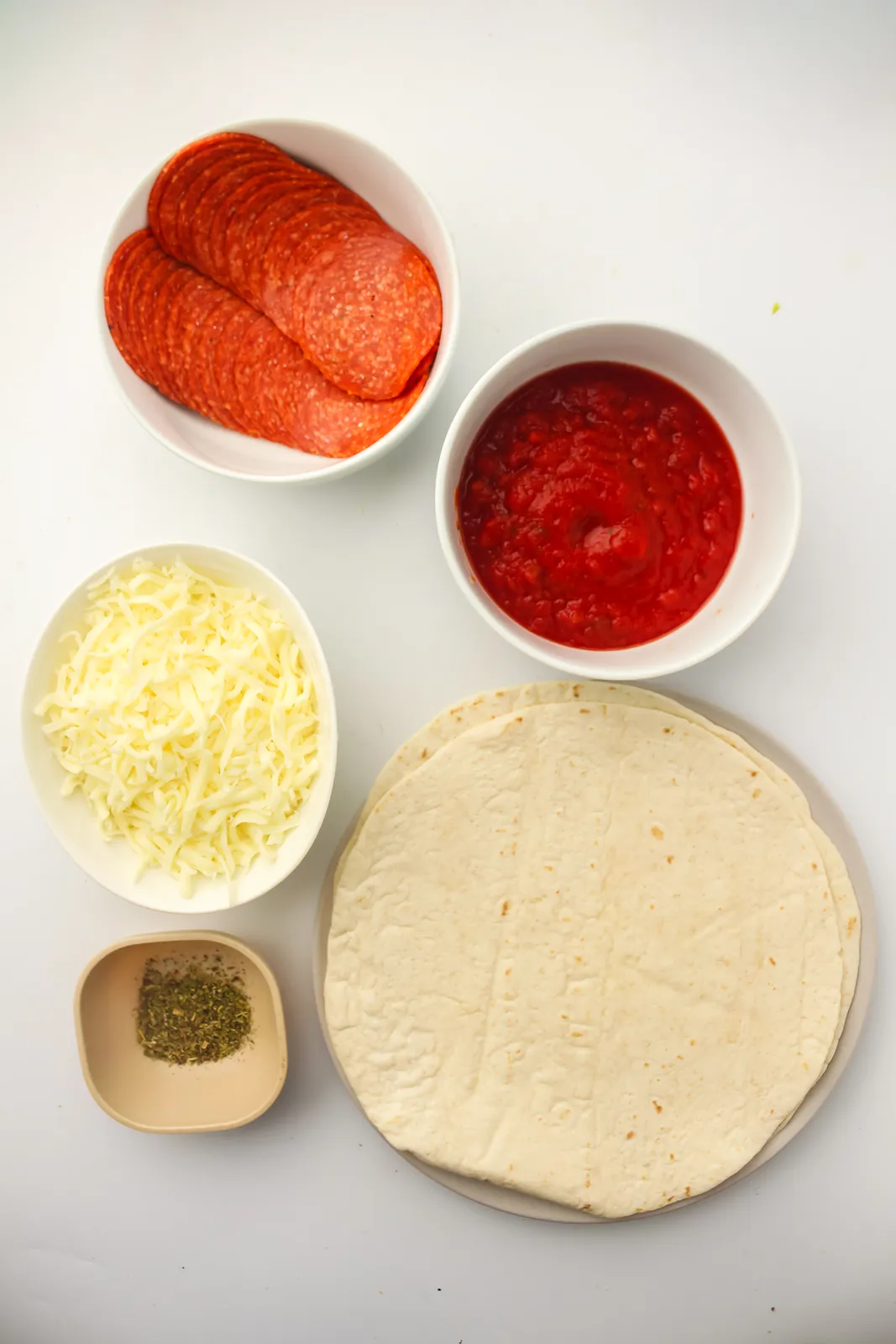 Ingredients for tortilla pizza: pepperoni slices, shredded mozzarella, pizza sauce, flour tortillas and Italian seasoning