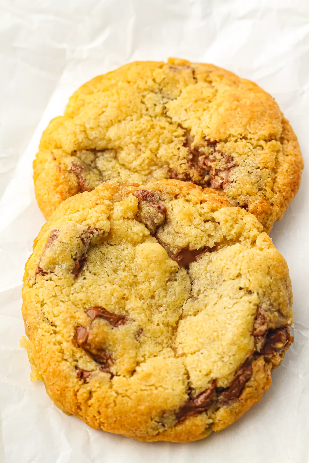 Two thick, crackled chocolate chunk rounds on crumpled parchment