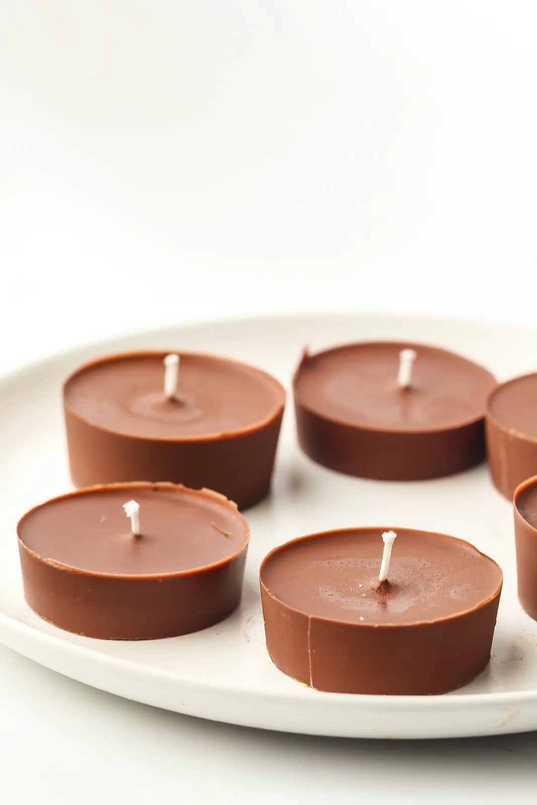 Unlit milk chocolate tealights with white wicks on a white plate