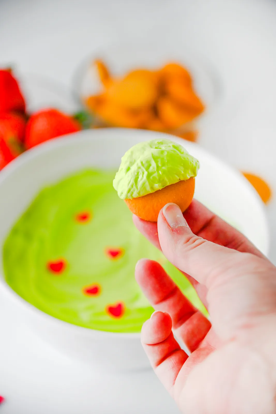 A vanilla wafer topped with bright green fluff held over the bowl